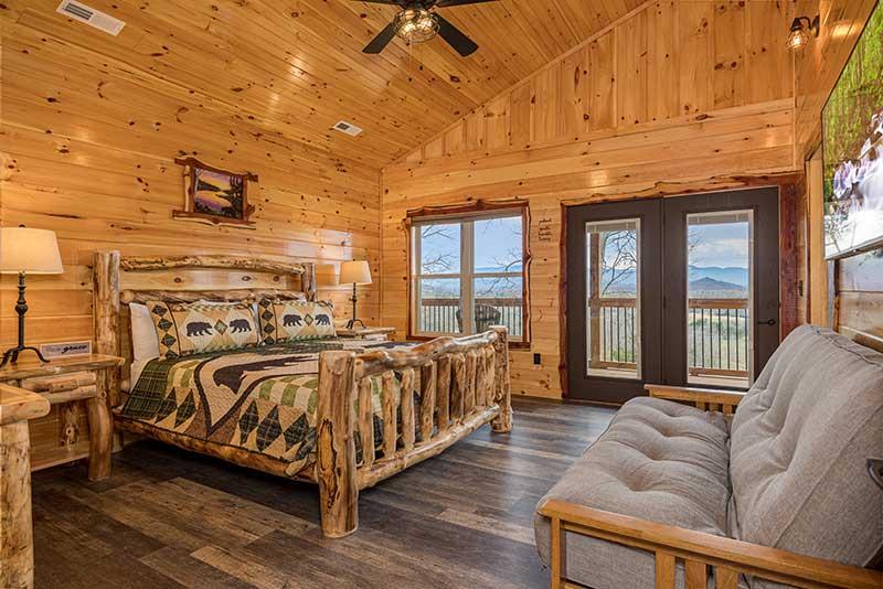 Rental cabin's master bedroom with king size log bed, tv, seating and porch walkout. at Morning View in Gatlinburg TN